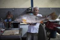 In this Sept. 1, 2019 photo, a vendor poses holding an Amazon fish known as "Pescada Branca" at the Ver-o-Peso riverside market in Belém, Brazil. The noisy, crowded and colorful market is the icon of a city that was once known for the rubber trade but that is now best known as the Amazon's culinary capital. (AP Photo/Rodrigo Abd)