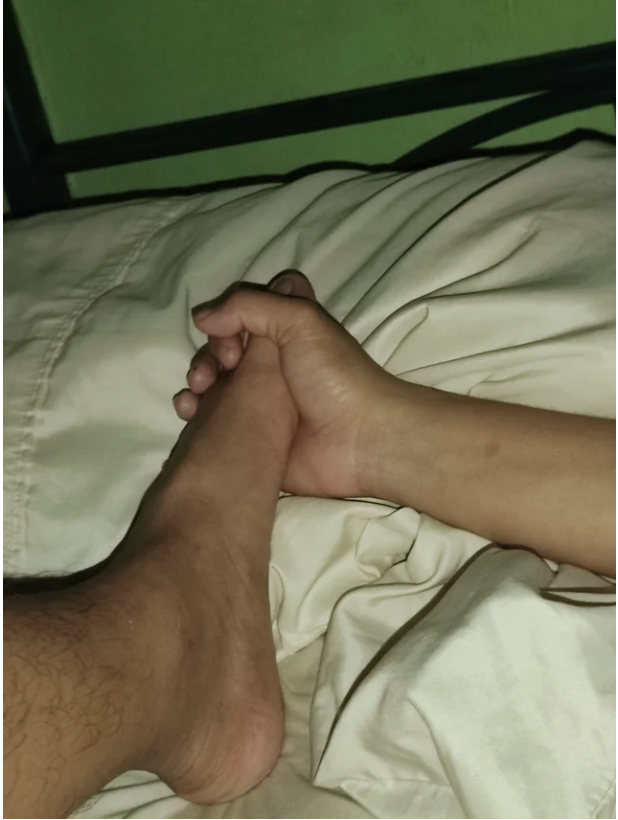 A hand holding a foot in bed