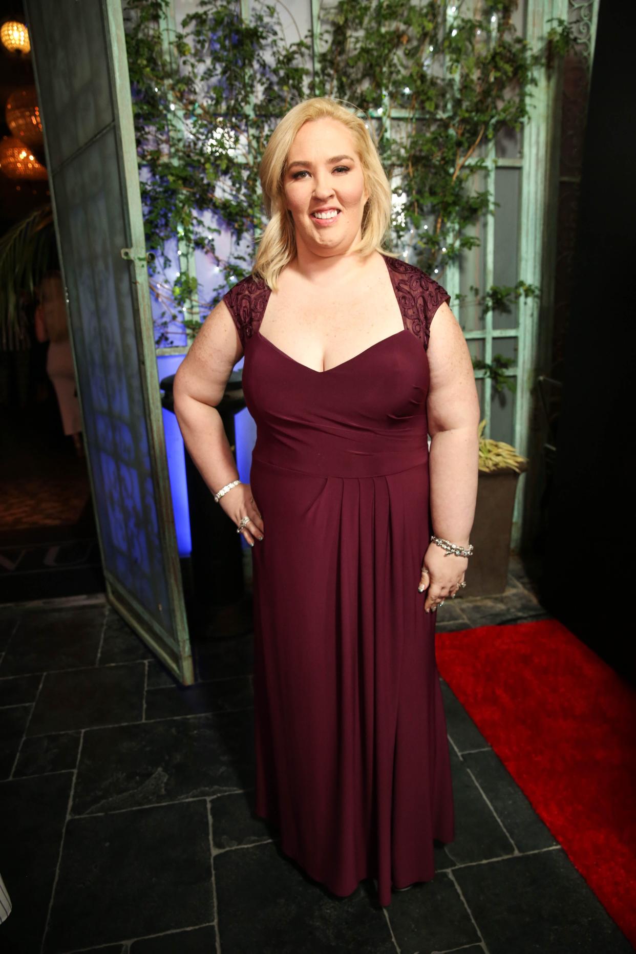 Mama June Shannon poses with her hand on her hip wearing a red gown