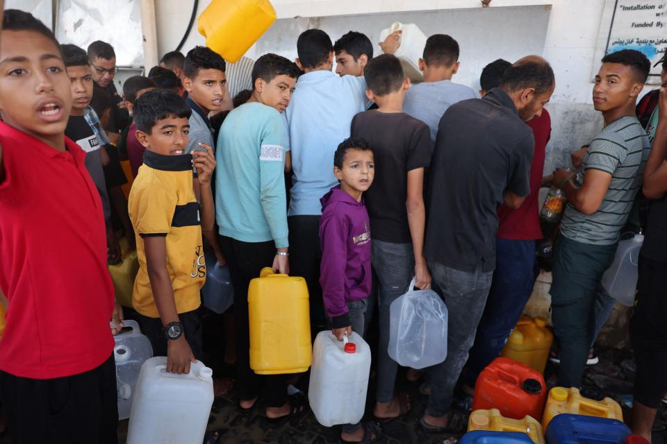 Palestinains boys and men holding containers, wait to collect portable water, in Khan Yunis, in the southern Gaza Strip on Oct. 26, amid the ongoing battles between Israel and the Palestinian group Hamas.