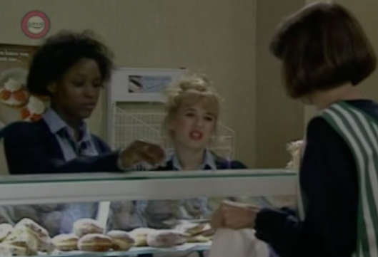 A still of Sharon in "2Point4 Children," she's next to a blonde actress and faces Belinda Porter, whose back is to the camera, they're in a bakery