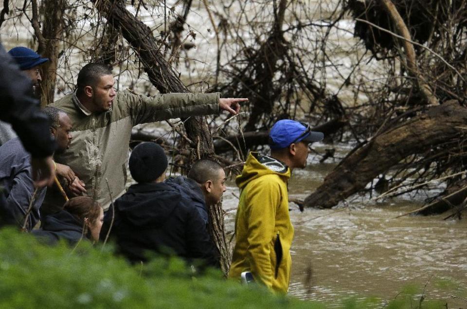A man points as the parents and friends of a missing 18-year-old woman look at what they believe to be their daughter's submerged car in Alameda Creek on Monday, Jan. 23, 2017, near Fremont, Calif. The unidentified woman's car plunged into rushing waters after colliding with another vehicle on Saturday, Jan. 21, 2017, and she is suspected of being in the submerged vehicle. (AP Photo/Ben Margot)