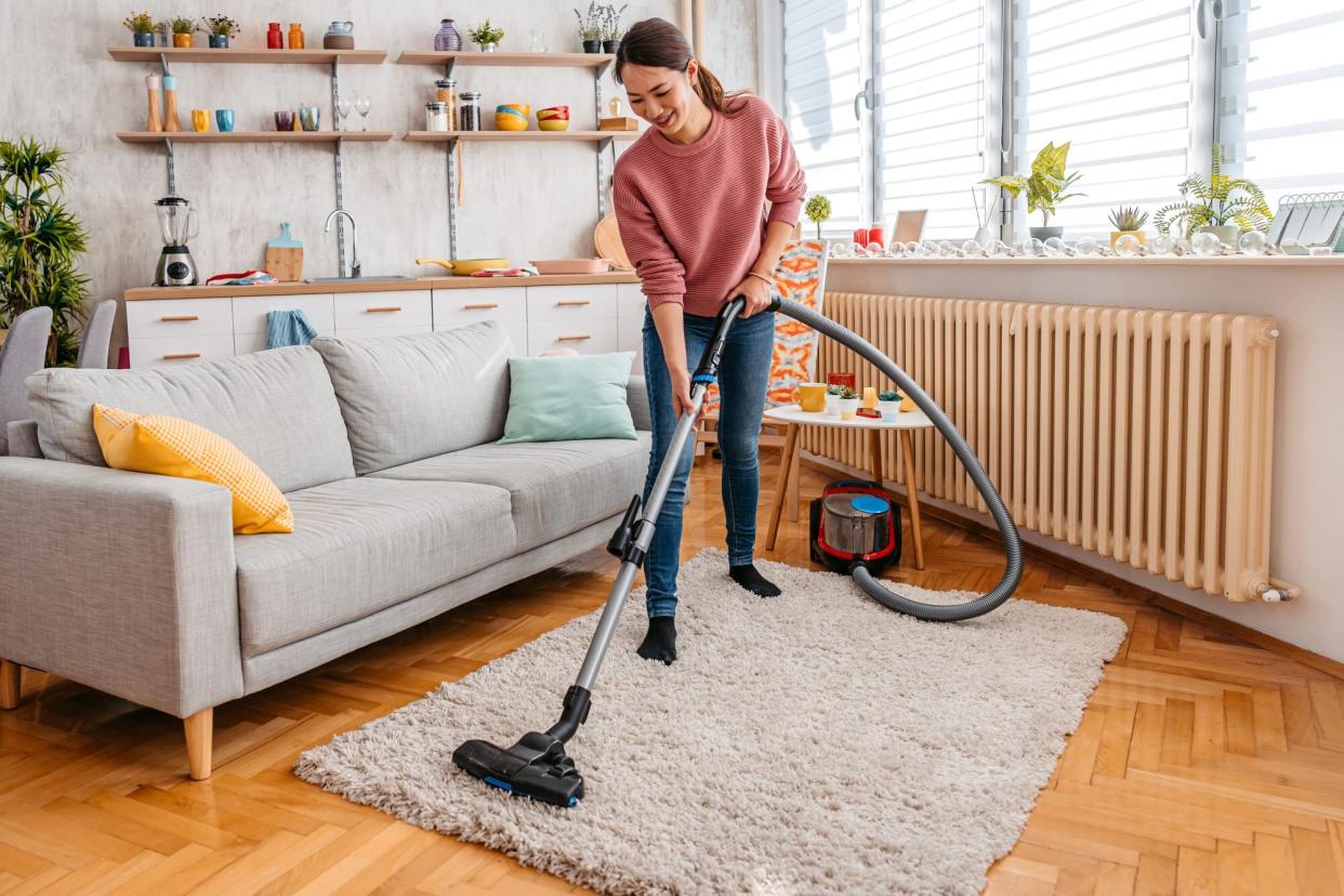 Woman vacuuming wool rug in apartment