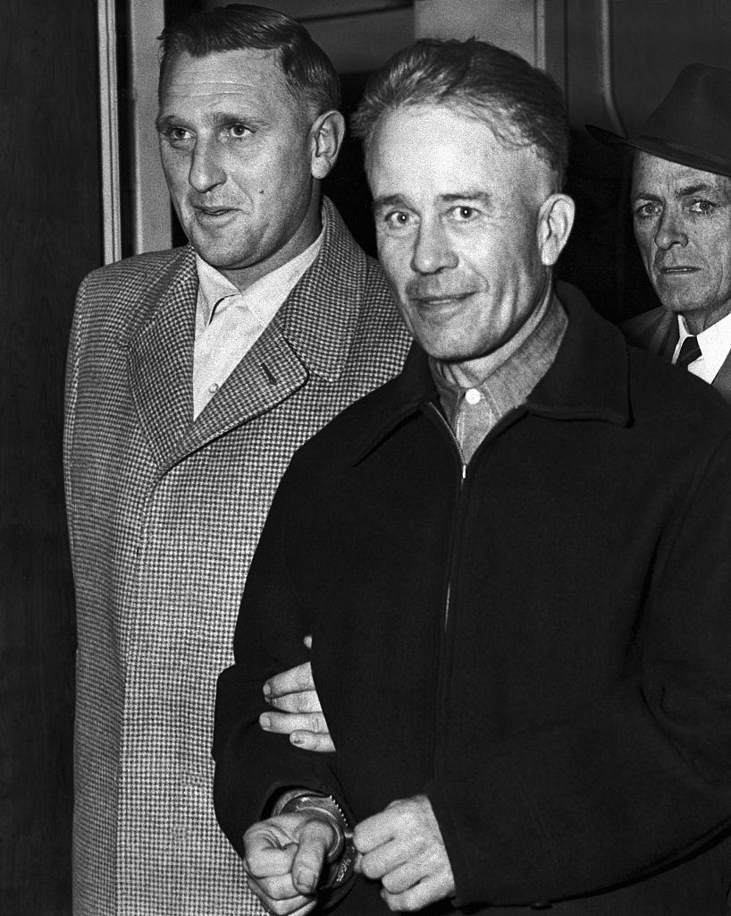 Two men in vintage attire, one in a checkered coat and the other in a dark jacket, walking side by side