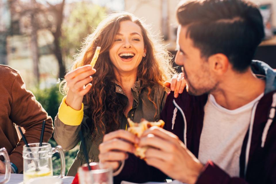 People sitting around a dinner table eating a meal together, with one holding a french fry.