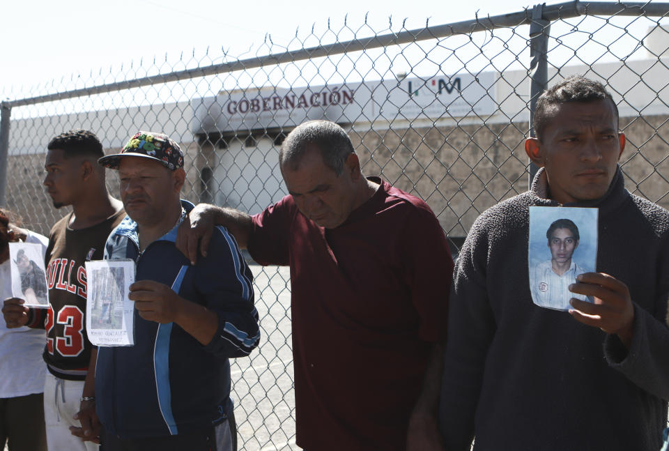 FILE - Migrants, mostly from Venezuela, hold photos of those who died in a fire at a Mexican immigration detention center, behind, during a prayer vigil outside the center in Ciudad Juarez, Mexico, April, 27, 2023. Four months after a fire in a Mexican immigration detention center at the border killed 40 migrants, some survivors are living in limbo at a Mexico City hotel, recovering from their injuries and awaiting the prosecution of their captors. (AP Photo/Christian Chavez, File)