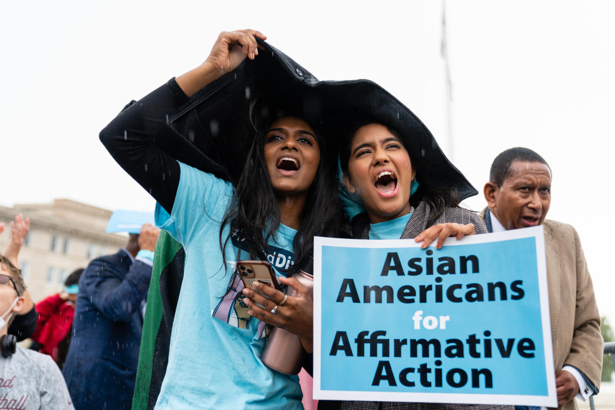 Two young women hold a raincoat over their heads to keep themselves dry, with a sign saying Asian Americans for Affirmative Action.