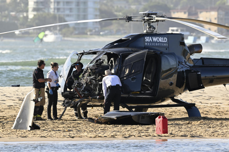 Emergency workers inspect a helicopter at a collision scene near Seaworld, on the Gold Coast, Australia, Monday, Jan. 2, 2023. Two helicopters collided killing several passengers and critically injuring a few others in a crash that drew emergency aid from beachgoers enjoying the water during the southern summer. (Dave Hunt/AAP Image via AP)