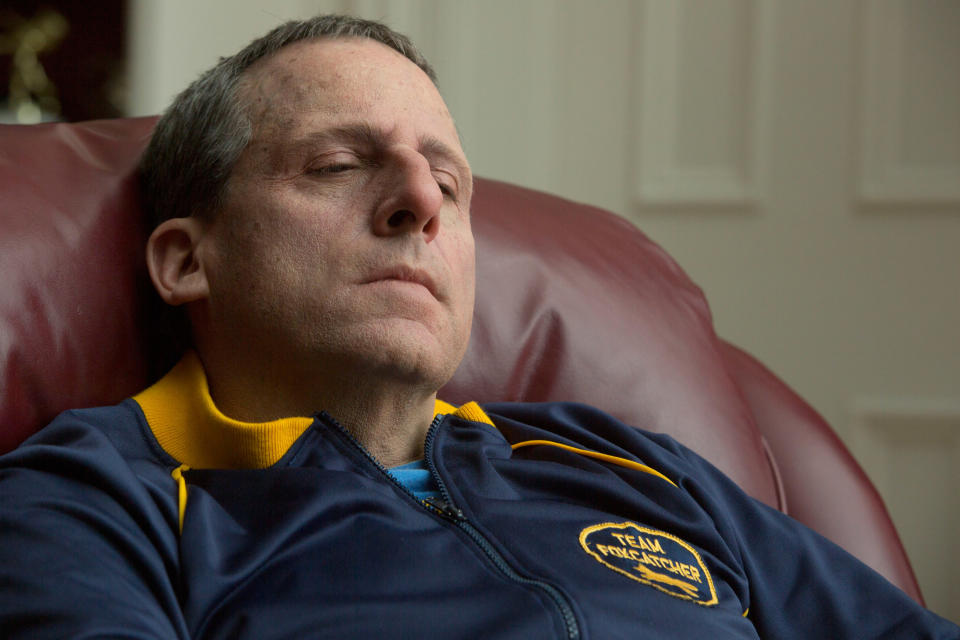 Steve Carell in heavy prosthetic makeup lounges on a chair