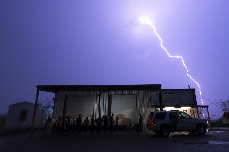 A lightning bolt is seen in the sky during a storm as migrants are lined up as they are processed by immigration officials outside the Starr County precinct 2 building after they crossed the Texas-Mexico border early Saturday, May 13, 2023, in Fronton, Texas. (AP Photo/Julio Cortez)