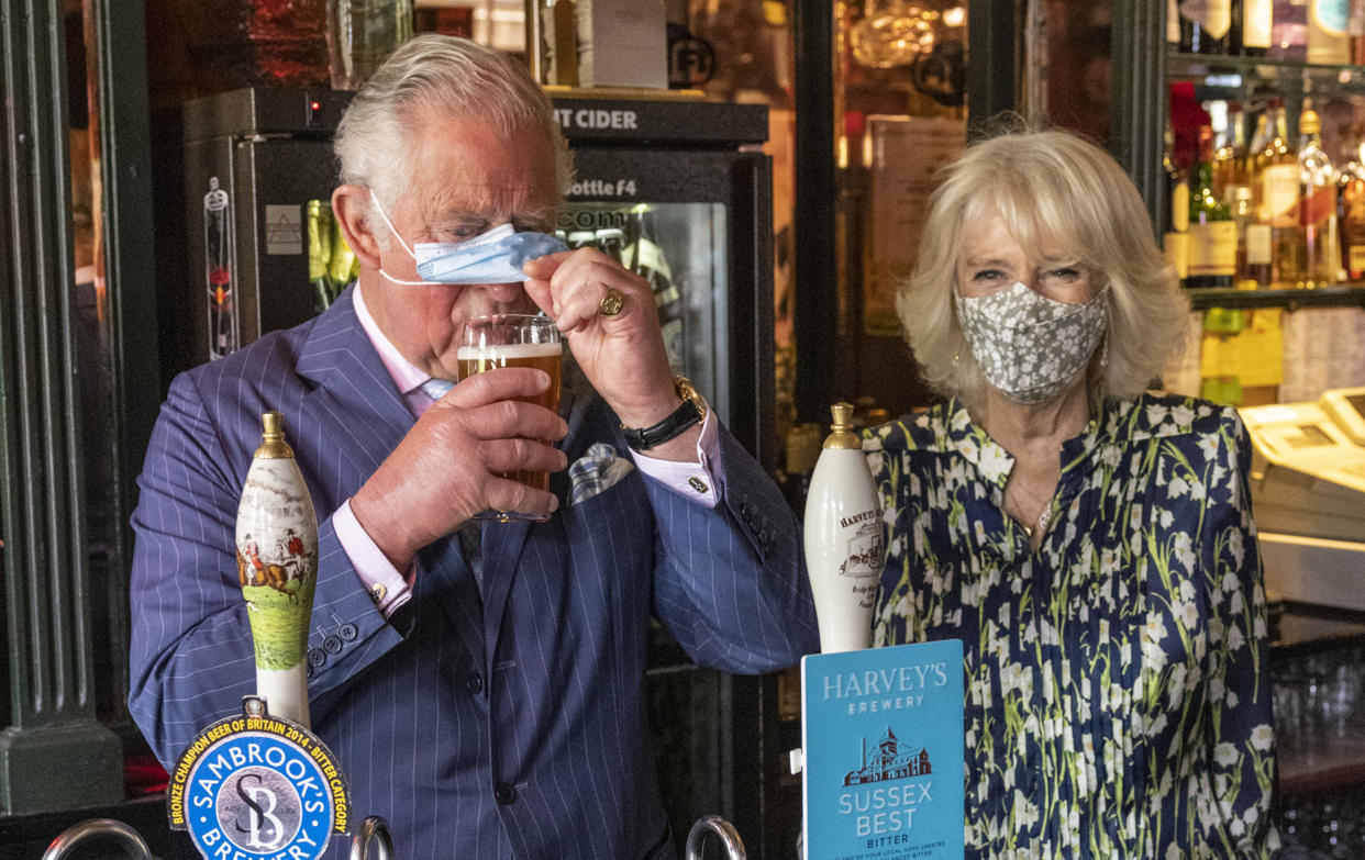 CLAPHAM, ENGLAND - MAY 27: Prince Charles, Prince of Wales adjusts his face mask to enable him to sip a pint that he pulled in a pub alongside Camilla, Duchess of Cornwall during a visit to Clapham Old Town on May 27, 2021 in Clapham, England. (Photo by Heathcliff O'Malley - WPA Pool/Getty Images)