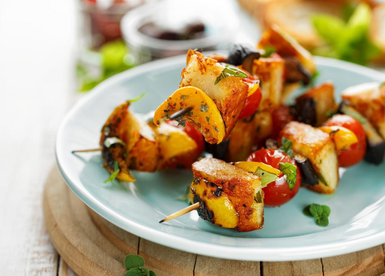 Grilled skewers of halloumi cheese and vegetables with addition aromatic herbs on a ceramic plate, delicious vegetarian food