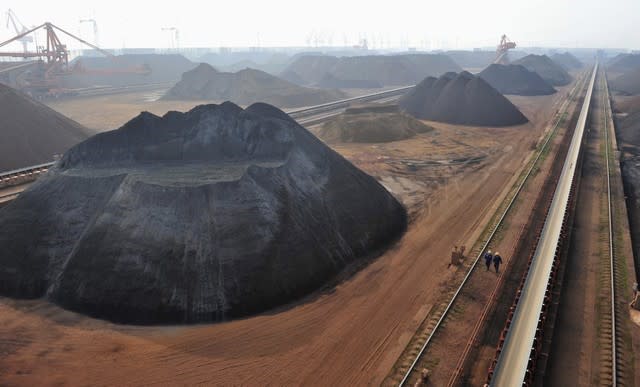 Workers walk past an iron ore storage site at Yingkou Port