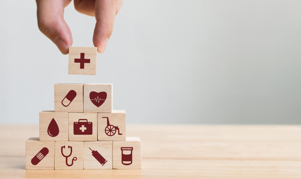 Hand placing a wood block on top of a pyramid of wood blocks, all of which have healthcare-related images printed on them