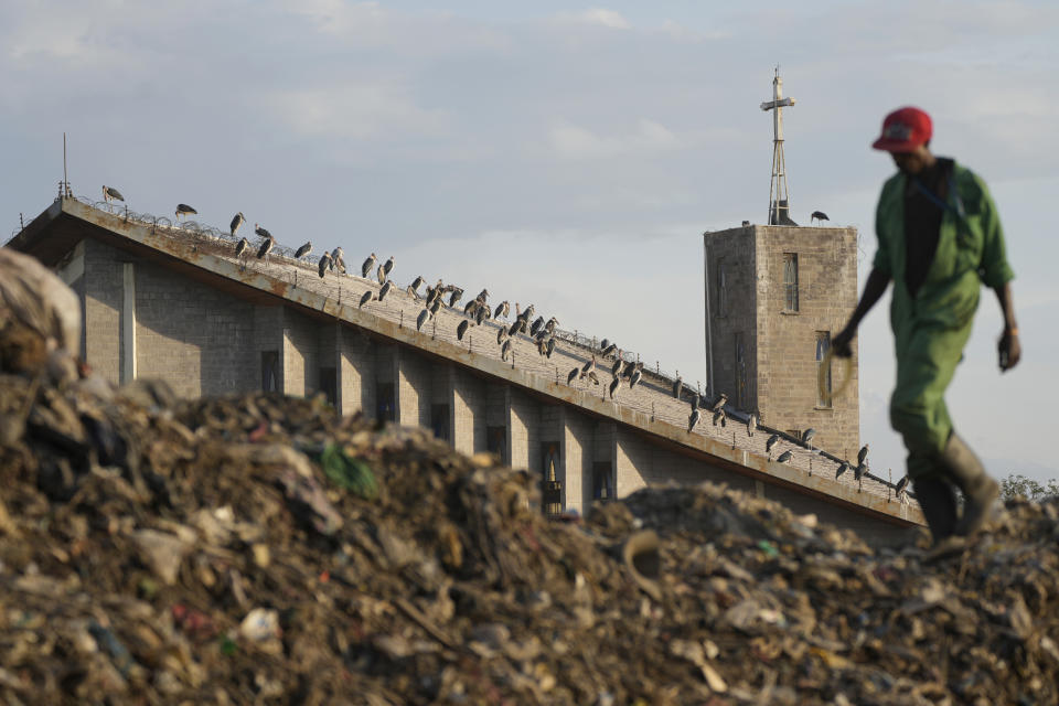 A man who scavenges recyclable materials for a living, walks past Marabou storks on a roof of a church at Dandora, the largest garbage dump in the capital Nairobi, Kenya Wednesday, March 20, 2024. U.N. agencies have warned that electrical and electronic waste is piling up worldwide while recycling rates continue to remain low and are likely to fall even further. (AP Photo/Brian Inganga)