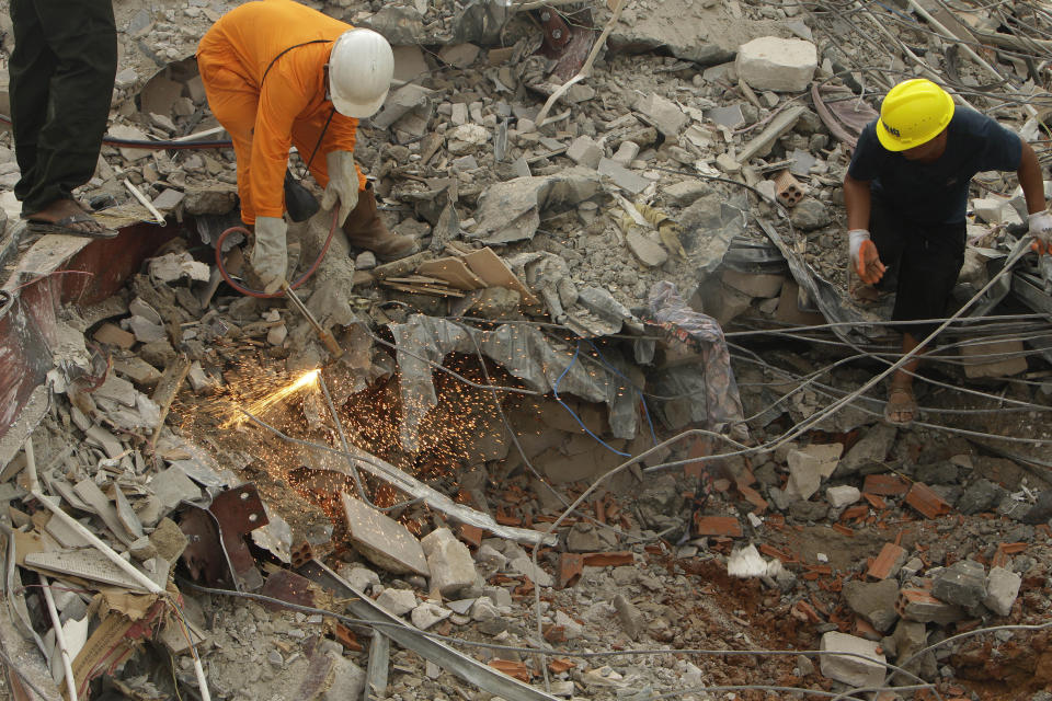 Rescuers try to remove the rubble at the site of a collapsed building in Preah Sihanouk province, Cambodia, Sunday, June 23, 2019. Rescue workers were using saws to cut steel beams and excavators to move piles of rubble of the collapsed seven-story building. (AP Photo/Heng Sinith)