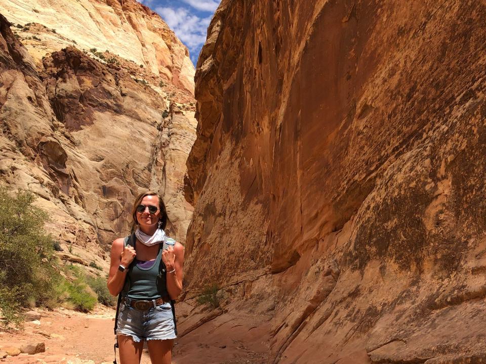 Emily, wearing a tank top, shorts, and sunglasses, hikes through red rock formations at Capitol Reef National Park.