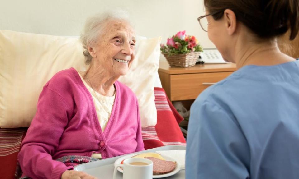 Care worker handing a tray of food to an older woman.