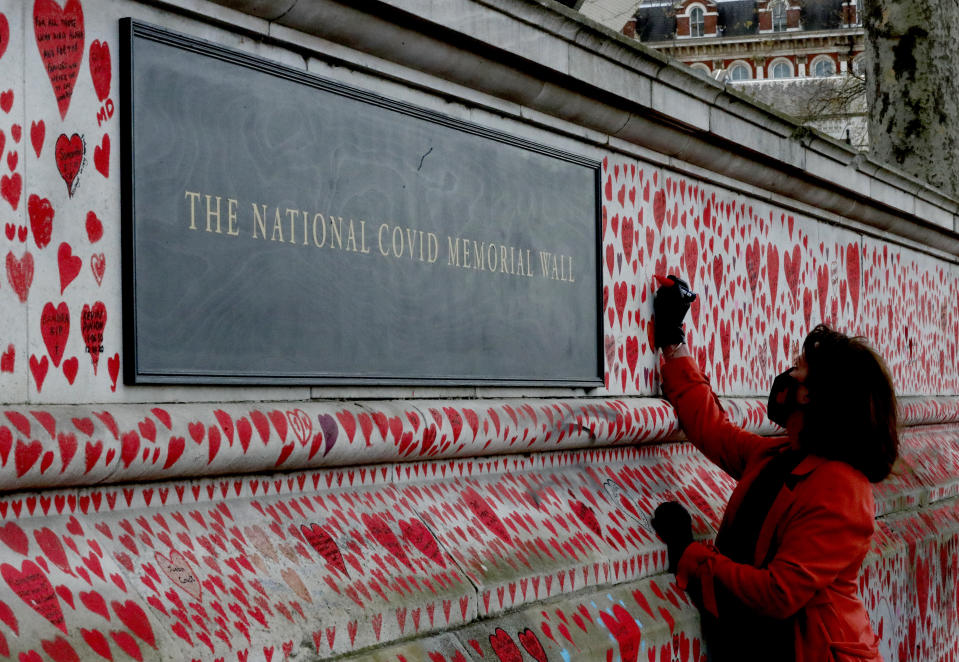 Fran Hall draws one of the last hearts as people paint red hearts to complete the approximately 150,000 hearts being painted onto the National Covid Memorial Wall to commemorate all those who have died of coronavirus, on the Thames Embankment opposite the Houses of Parliament in London, Thursday, April 8, 2021. Bereaved families want the wall of painted hearts to remain a site of national commemoration and are asking the Prime Minister to help make the memorial permanent. (AP Photo/Frank Augstein)