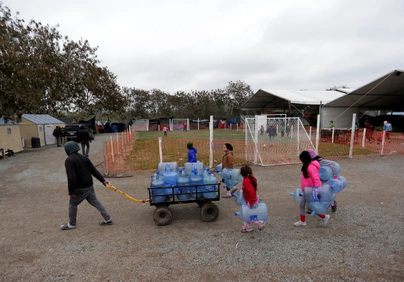 Imagen de archivo de personas llevando bidones de agua vacíos en el campamento migratorio de Matamoros, México.