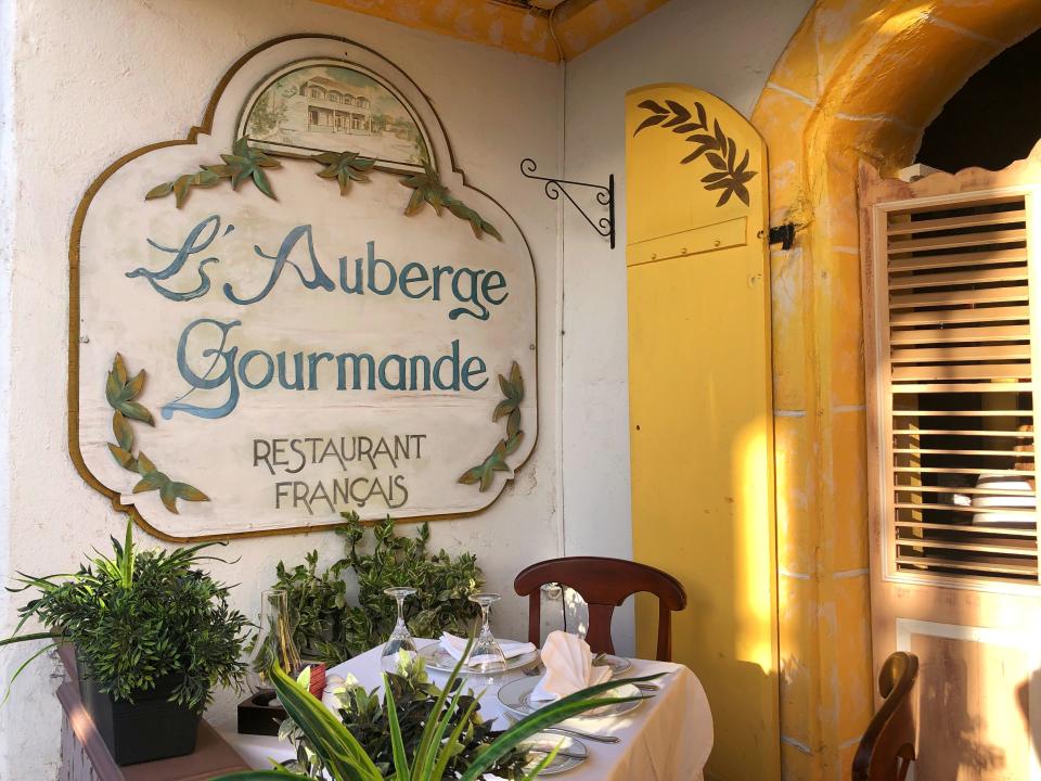 A sign reading L'Auberge Gourmande above a small table.