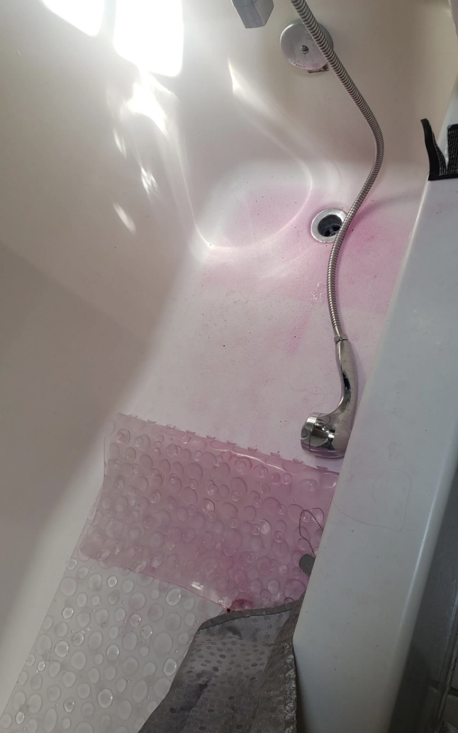 Bathroom with a bathtub partially filled with water and a non-slip mat; there is reflective light on the surface