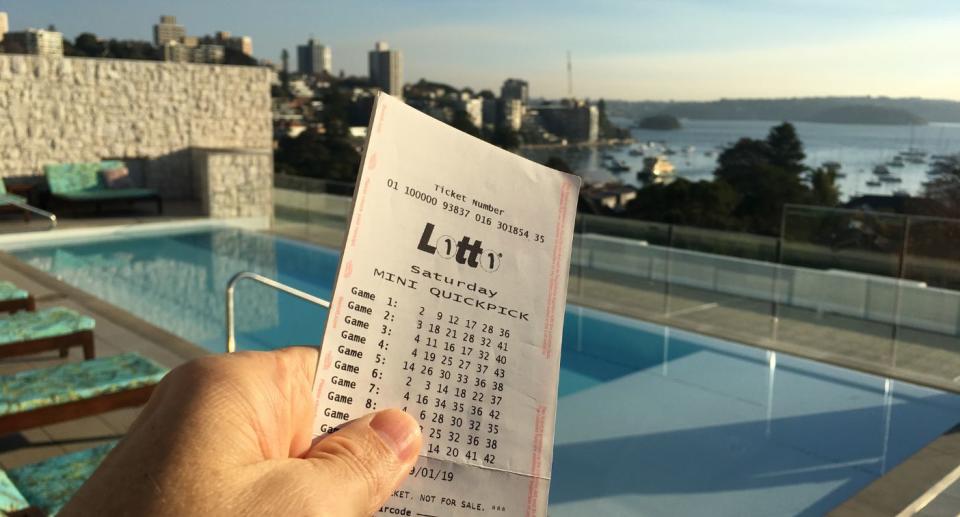 Saturday Lotto winner ticket held up in front of pool and harbour view