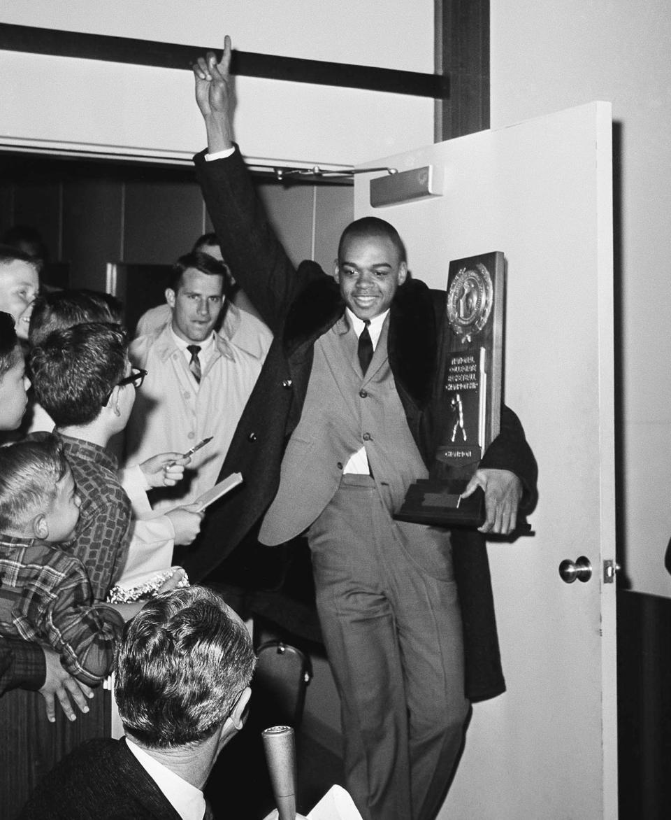 FILE - UCLA's Walt Hazzard carries the NCAA college basketball championship trophy as the team arrives from Kansas City at the airport in Los Angeles, March 23, 1964. (AP Photo/Harold Matosian, File)