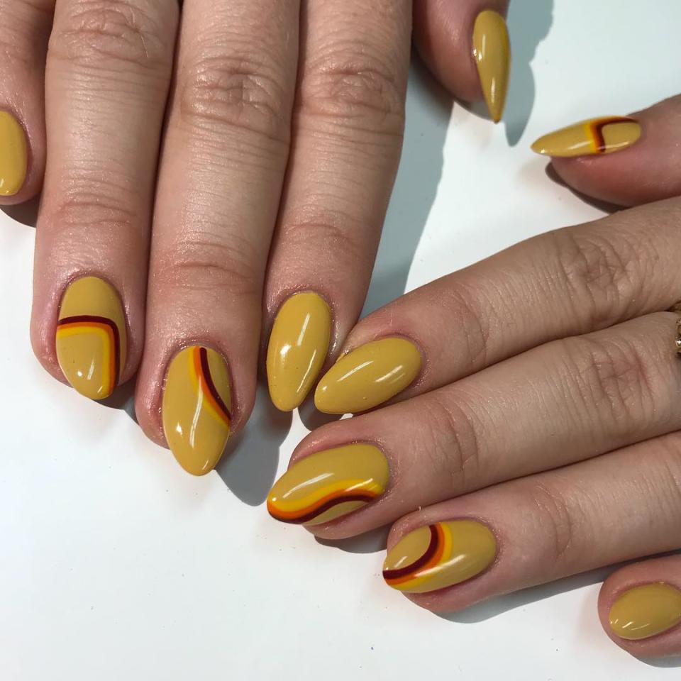 "I just love warm tones," nail artist <a href="https://www.instagram.com/p/BqXdVYSAGX4/" rel="nofollow noopener" target="_blank" data-ylk="slk:Savannah Walker;elm:context_link;itc:0;sec:content-canvas" class="link ">Savannah Walker</a> tells <em>Allure</em> of how she decided on the shades in this retro manicure. The burgundy, orange, and yellow stripes on a mustard base make it not only '70s-inspired but also ideal for fall.