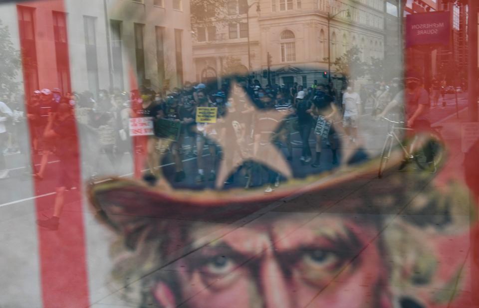 TOPSHOT - Demonstrators are seen in the reflexion of a classic WW1 US Army recruitment poster, as protests triggered by the death of George Floyd while in police custody, continue on June 23, 2020, in Washington, DC. - US President Trump on his way to Arizona warned that protesters who attempted to establish an "autonomous zone" in the US capital would be met with "serious force," following a night of protests at Lafayette Square where a crowd of protestors tried to topple the statue of Jackson. (Photo by Brendan Smialowski / AFP) (Photo by BRENDAN SMIALOWSKI/AFP via Getty Images)