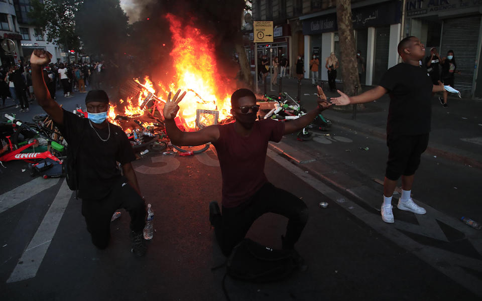 Protesters kneel and react by a burning barricade during a demonstration Tuesday, June 2, 2020 in Paris. Paris riot officers fired tear gas as scattered protesters threw projectiles and set fires at an unauthorized demonstration against police violence and racial injustice. Several thousand people rallied peacefully for two hours around the main Paris courthouse in homage to George Floyd and to Adama Traore, a French black man who died in police custody. (AP Photo/Michel Euler)