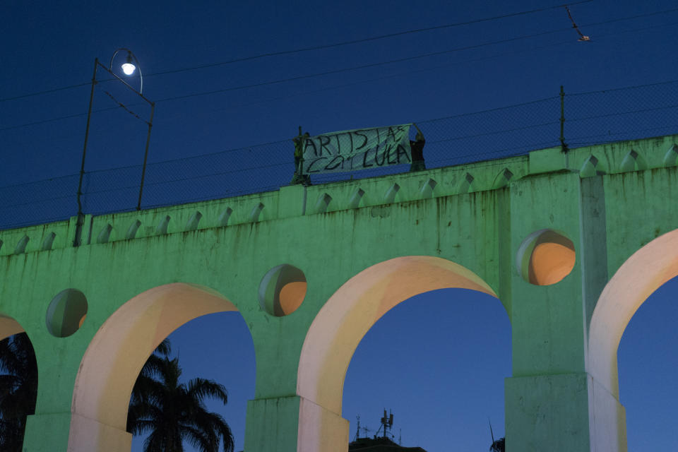 People place a banner with a message that reads in Portuguese: "Artists with Lula" over the Carioca Aqueduct, also know as Arcos da Lapa, during the Lula Free festival, in Rio de Janeiro, Brazil, Saturday, July 28, 2018. Popular Brazilian musicians and social movements organized a concert to call for the release of Brazil's former president Luiz Inacio Lula da Silva, who has been in prison since April, but continues to lead the preferences on the polls ahead of October's election. (AP Photo/Leo Correa)