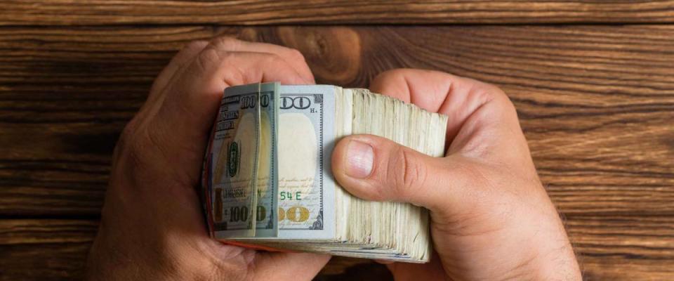 Man checking a thick stack of 100 dollar bills thumbing through them over a rustic wood table with copy space