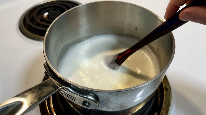 hand stirring warm milk in a pot with a wooden spoon