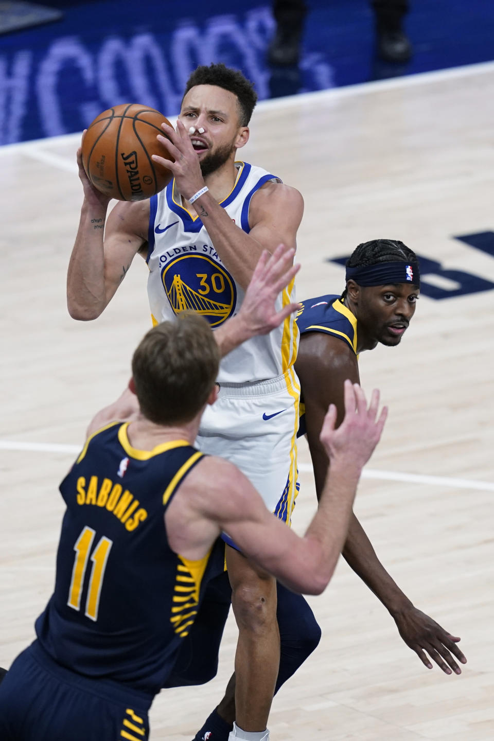 Golden State Warriors' Stephen Curry (30) shoots from between Indiana Pacers' Justin Holiday, right, and Domantas Sabonis during the second half of an NBA basketball game Wednesday, Feb. 24, 2021, in Indianapolis. (AP Photo/Darron Cummings)