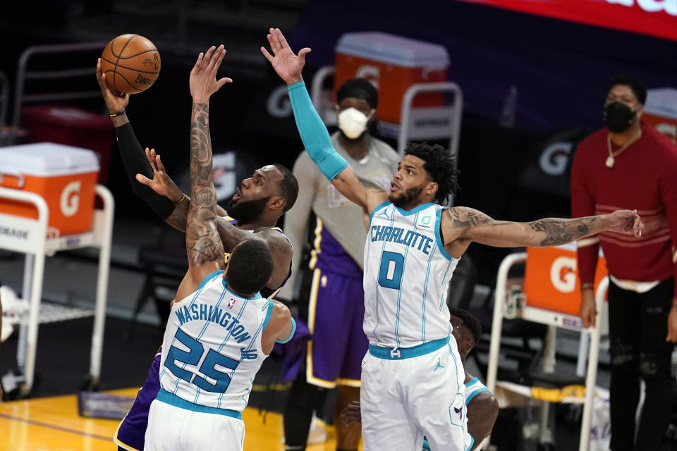 Los Angeles Lakers forward LeBron James, back left, scores past Charlotte Hornets forward P.J. Washington (25) and forward Miles Bridges (0) during the first half of an NBA basketball game Thursday, March 18, 2021, in Los Angeles. (AP Photo/Marcio Jose Sanchez)