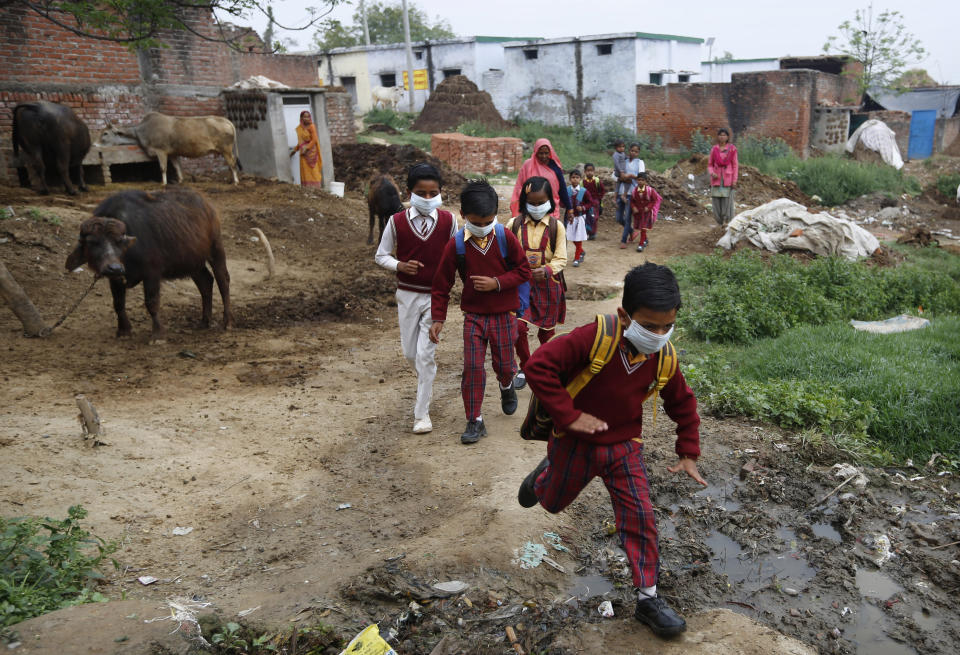 Children wearing face masks amid concerns over the spread of the coronavirus, return home after learning that public gatherings and schools are shut following a state government order, at a village in Kannauj, in India's most populous state of Uttar Pradesh, Saturday, March 14, 2020. (AP Photo/Rajesh Kumar Singh)