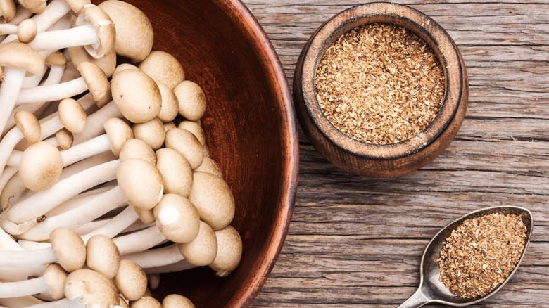 Top-down view of a bowl of fresh mushrooms, a bowl of mushroom powder, and a spoon