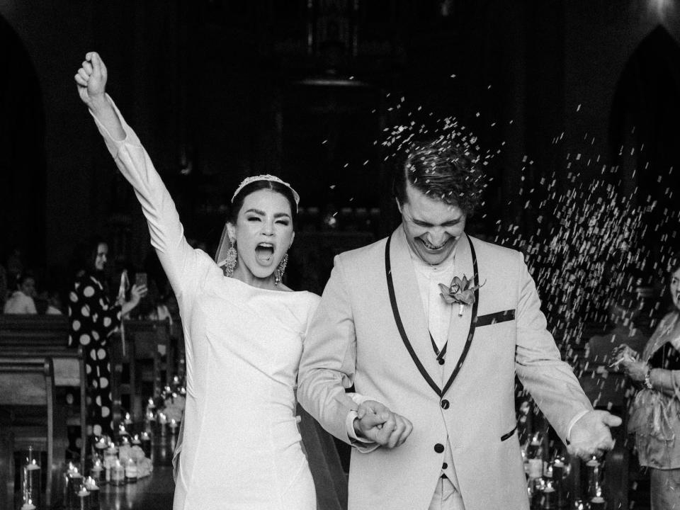 A bride raises her hand in triumph as she and the groom leave their wedding.