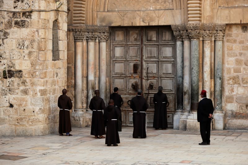 Roman Catholic monks pray in front of the locked door of Jerusalem's Church of the Holy Sepulchre amid coronavirus restrictions in the walled Old City