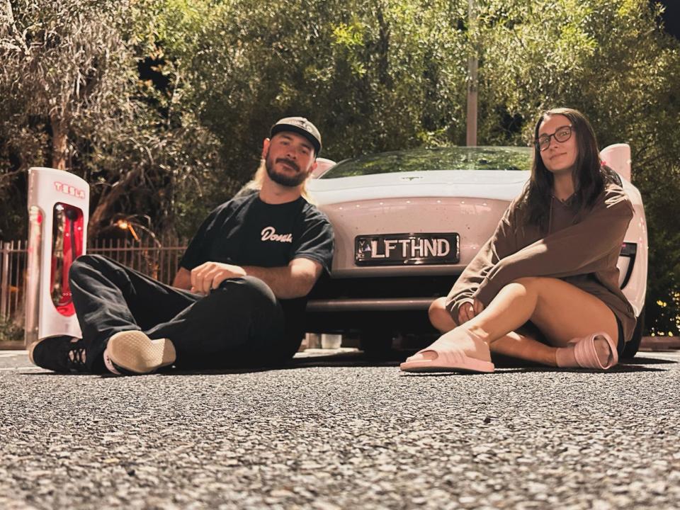 JJ and his friend Siouxsie sitting on the ground in front of the white Tesla. 