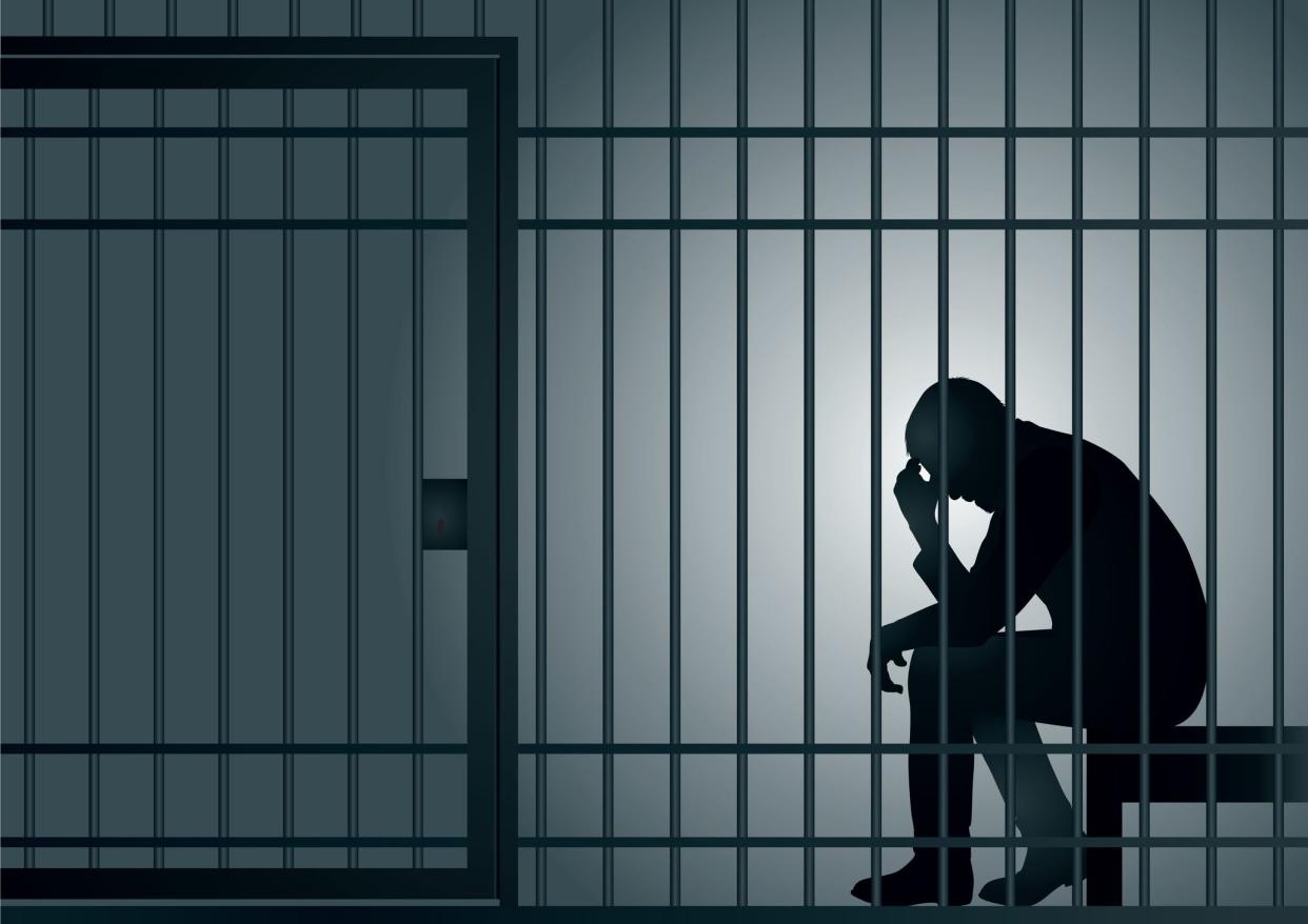 Concept of prison and arrest of an offender or criminal, with a prisoner sitting in his cell holding his head in his hands.