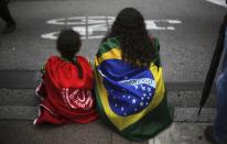 A woman and her daughter, wearing the Brazilian national flag (R) and the flag of Brazil's Roofless Workers Movement (MTST) on their backs respectively, sit on the street during a protest to demand for affordable low-income housing from the government in Sao Paulo December 11, 2013. REUTERS/Nacho Doce (BRAZIL - Tags: CIVIL UNREST POLITICS BUSINESS SOCIETY REAL ESTATE)