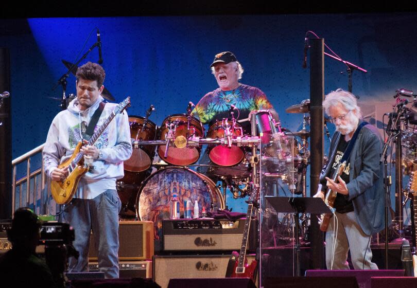 John Mayer on guitar, Bill Kreutzmann on drums and Bob Weir on guitar of Dead and Company playing on a stage