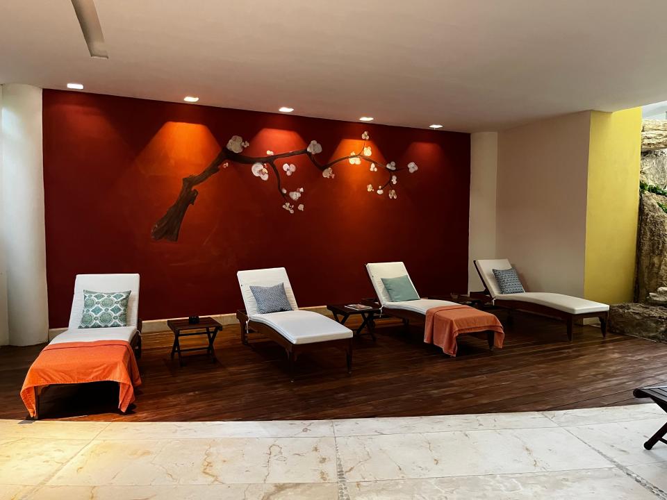 Spa with red walls with cherry blossom branch painted on and four lounge chairs, two with orange towels, in front