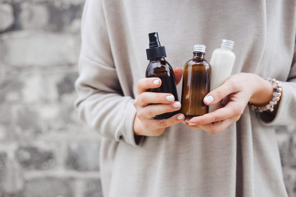 Woman holding bottles with spa cosmetics against gray wall. Photo: Getty Images.