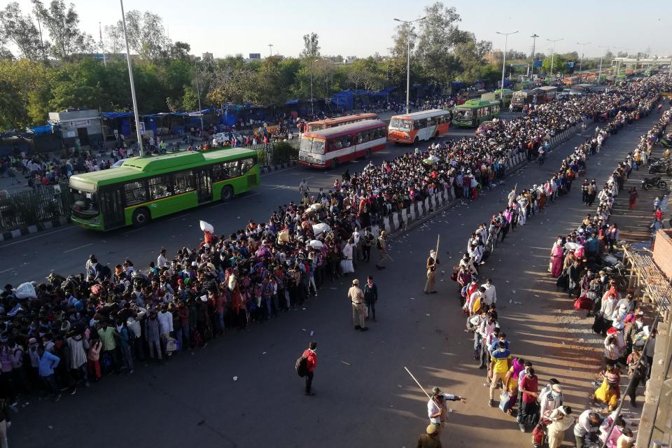 Migrant workers and their family members lineup outsdie the Anand Vihar bus terminal to leave for their villages during a government-imposed nationwide lockdown as a preventive measure against the COVID-19 coronavirus in New Delhi on March 28, 2020. - Tens of thousands of migrant workers and their famiies on March 28 fought and shoved their way onto buses organised by India's most populous state to get them to their home towns amid the coronavirus pandemic. (Photo by Bhuvan BAGGA / AFP) (Photo by BHUVAN BAGGA/AFP via Getty Images)