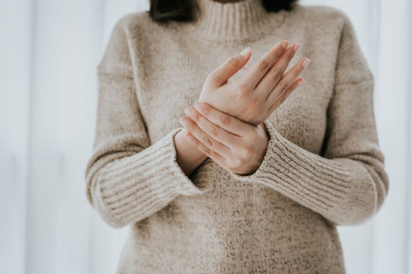 Cropped shot of woman in sweater holding her wrist pain