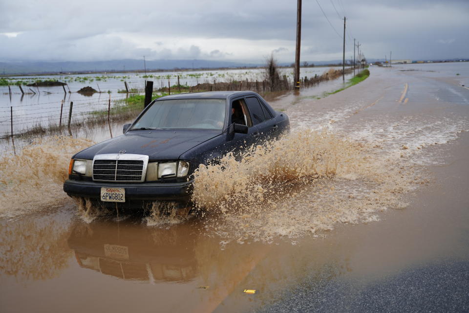 A car throws up brown water on a flooded farm road.