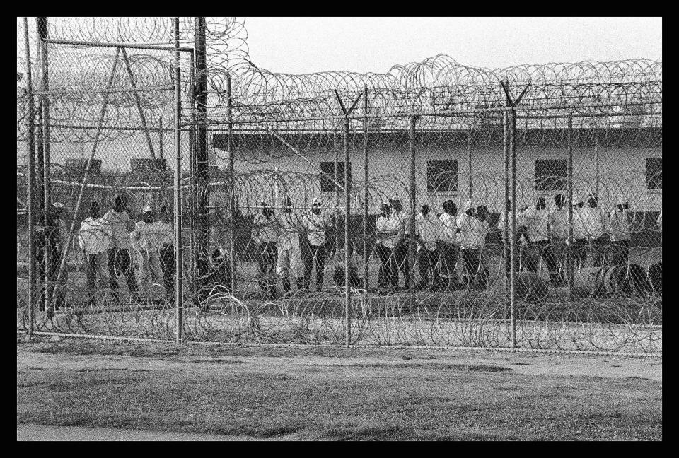 This 2004 photo shows prisoners lining up for work call in a yard behind fencing and razor wire at the Louisiana State Penitentiary in Angola, La. The former 19th-century antebellum plantation once was owned by one of the largest slave traders in the U.S. Today, it houses some 3,800 men behind its razor-wire walls. (Chandra McCormick via AP)